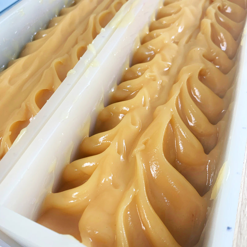 Freshly made Tupelo Honey and Rosewater soap in the mold. Light honey-colored textured soap glistening in the light in an opaque white silicone mold.